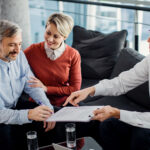 Happy mid adult couple signing a contract with their agent in th