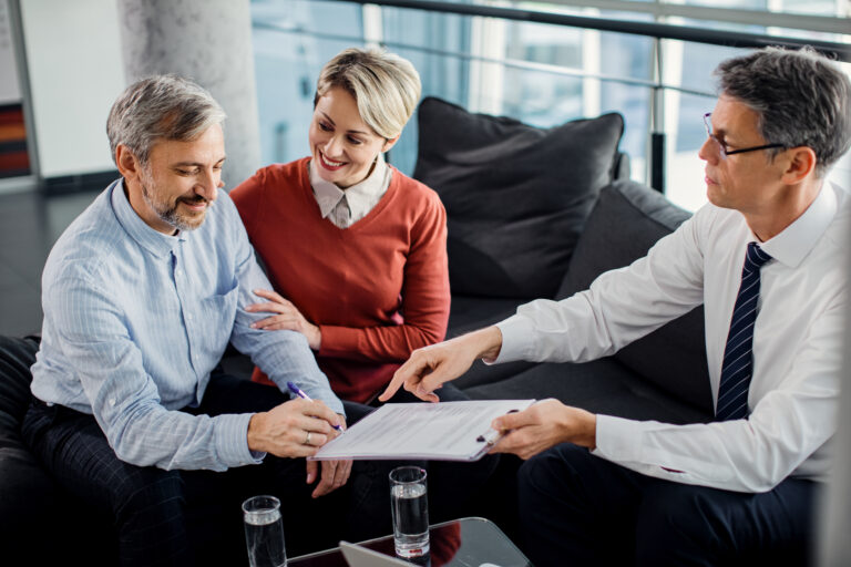 Happy mid adult couple signing a contract with their agent in th