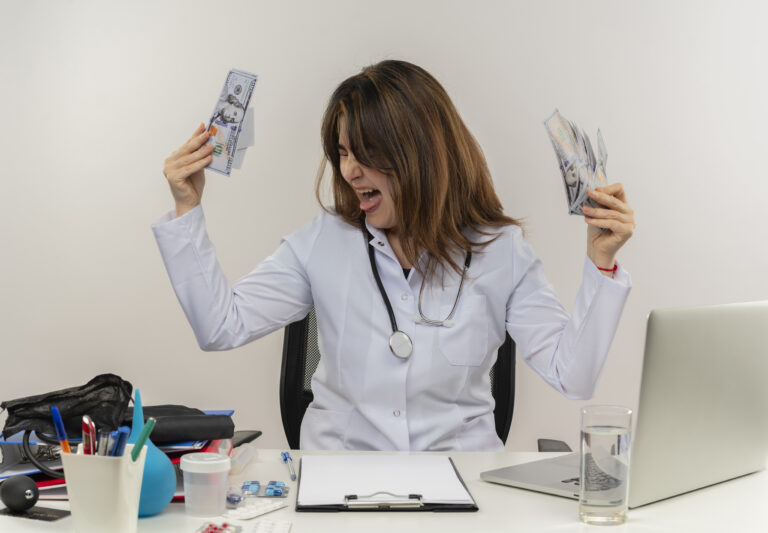 with closed eyes joyful middle-aged female doctor wearing wearing medical robe with stethoscope sitting at desk work on laptop with medical tools holding cash on isolated white backgroung with copy space