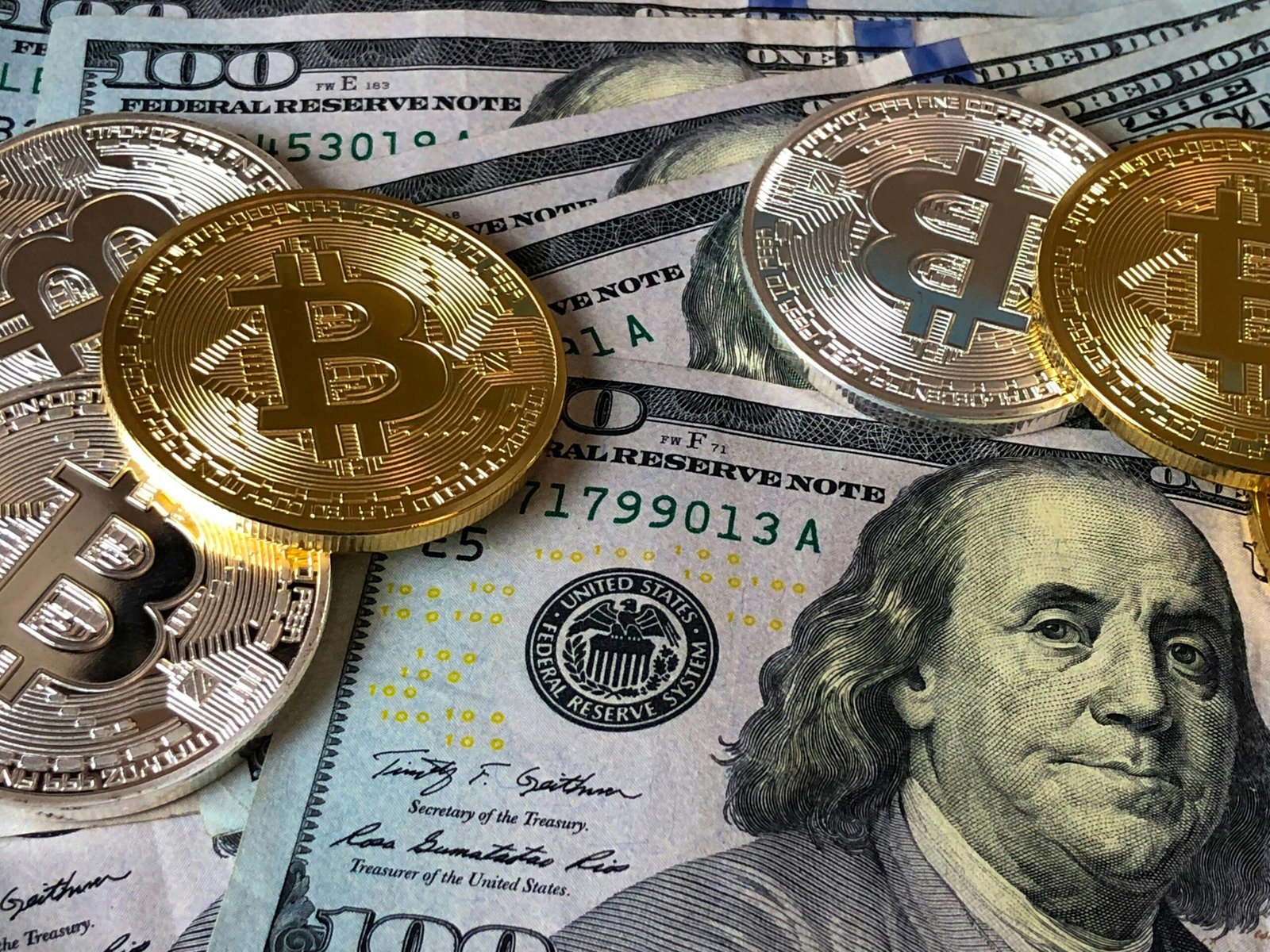 Bitcoin coins placed on U.S. hundred-dollar bills showing the relationship between crypto and traditional finance.