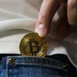 Person placing a Bitcoin coin into a jeans pocket, symbolizing digital wealth and investment.