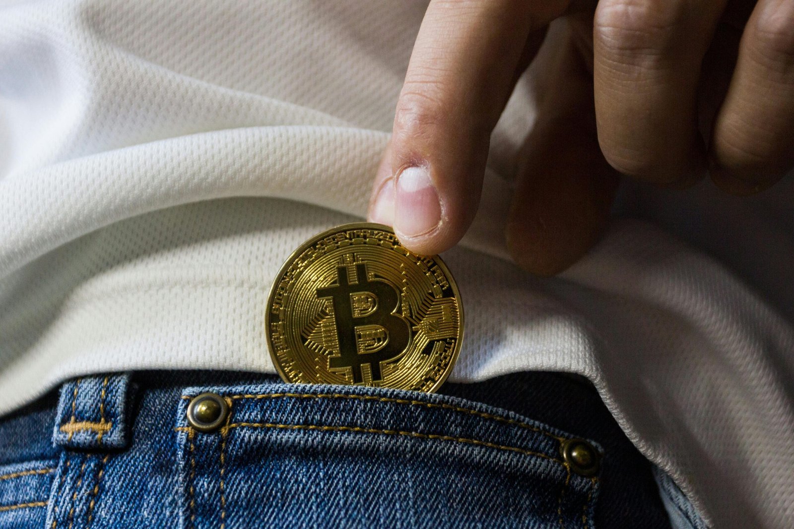 Person placing a Bitcoin coin into a jeans pocket, symbolizing digital wealth and investment.